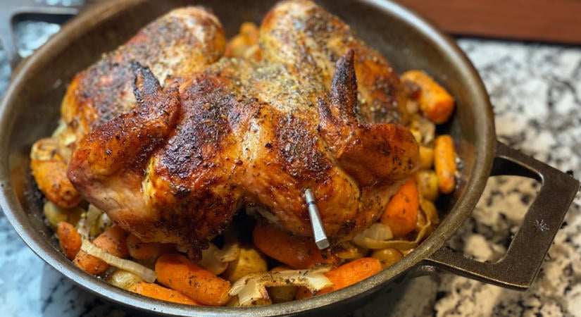 Egész csirke gyökérzöldségeken öntöttvasban a grillen